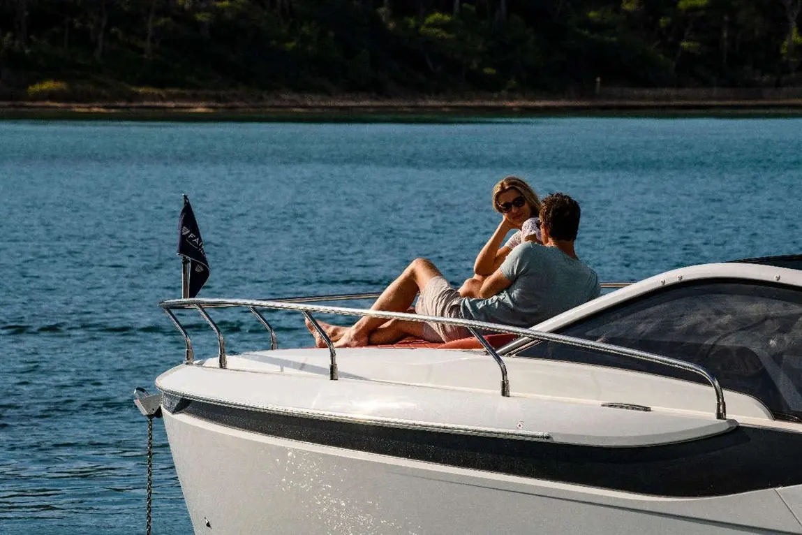 A couple relaxes on the bow of a boat, enjoying the serene blue waters and sunlight on a calm day.
